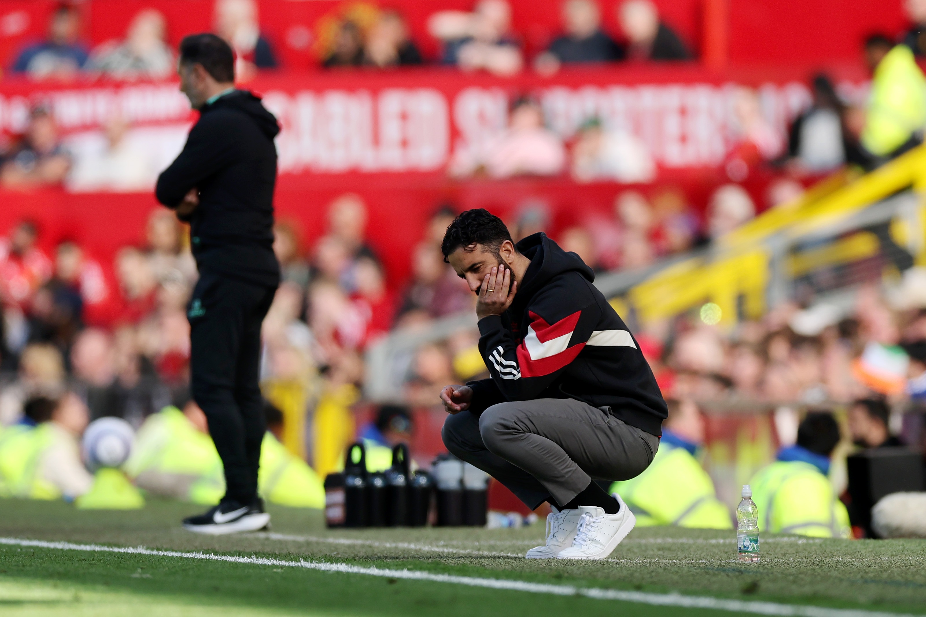 Manchester United head coach Ruben Amorim crouches on the touchline looking distraught.