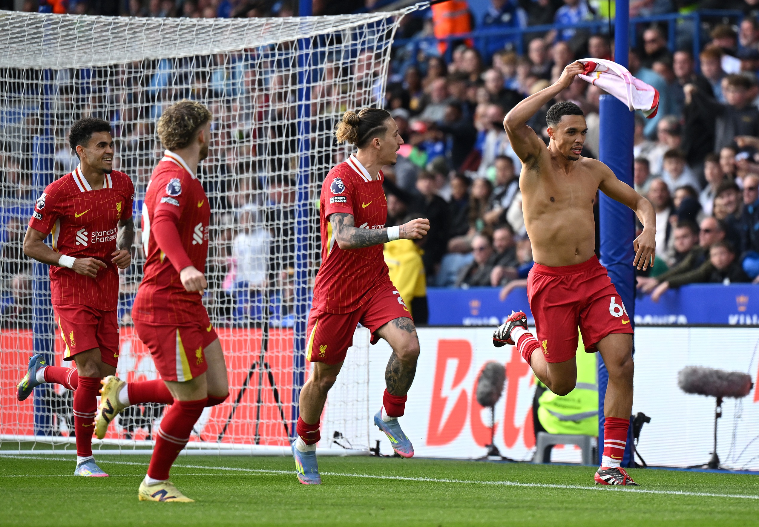 Trent Alexander-Arnold waves his shirt across his head next to Liverpool players.