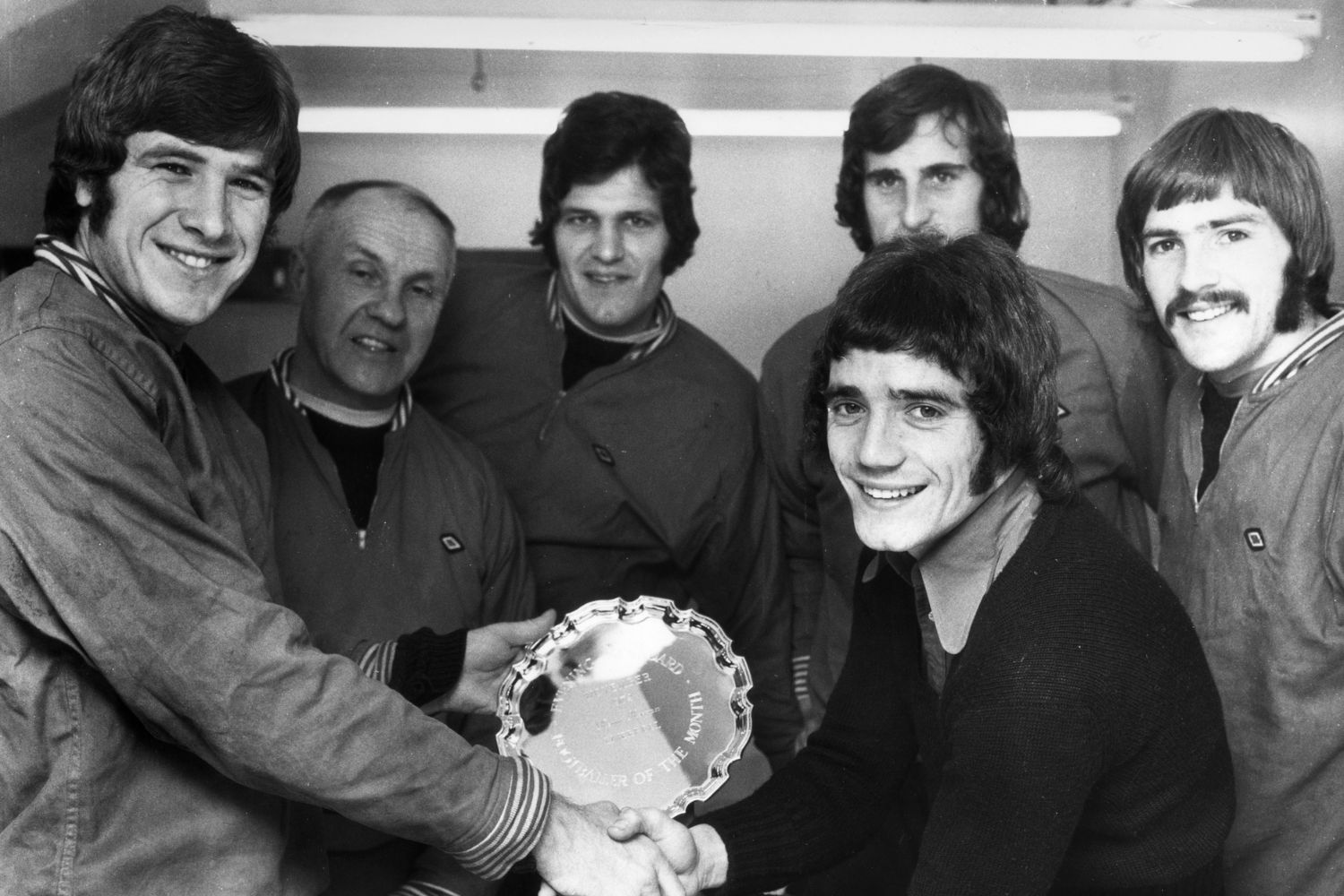 Emlyn Hughes presenting Kevin Keegan with the Evening Standard player of the month award. He is watched by manager Bill Shankly, John Toshack, Ray Clemence and Steve Heighway. The prize is an inscribed silver salver and he also received two magnums of Lanson Black Label Champagne.