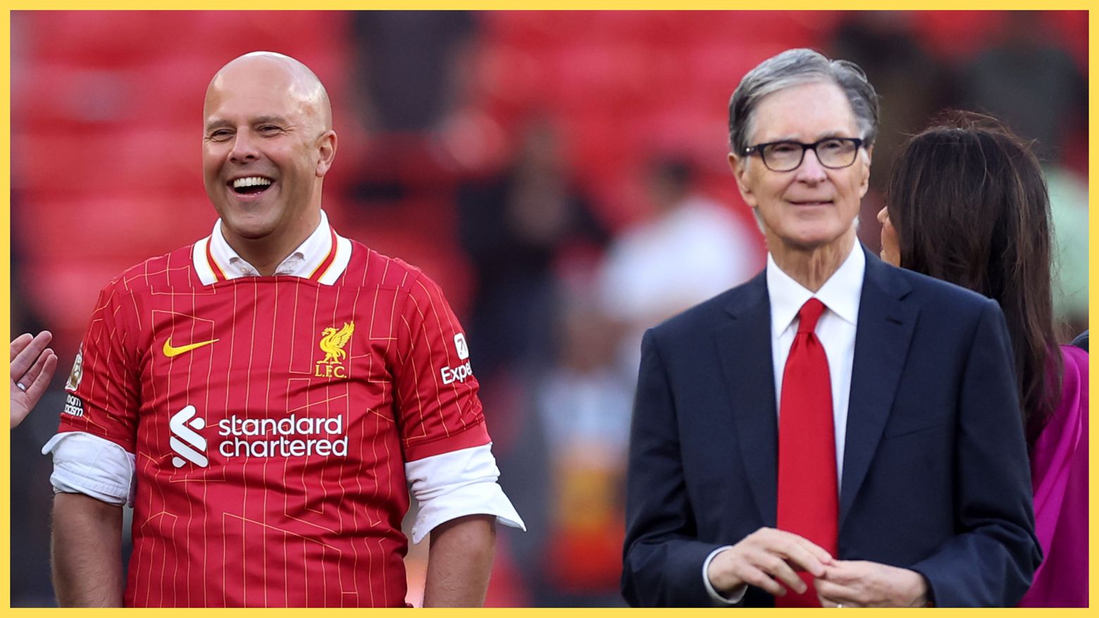 Arne Slot laughs next to a smiling John W Henry during Liverpool game.