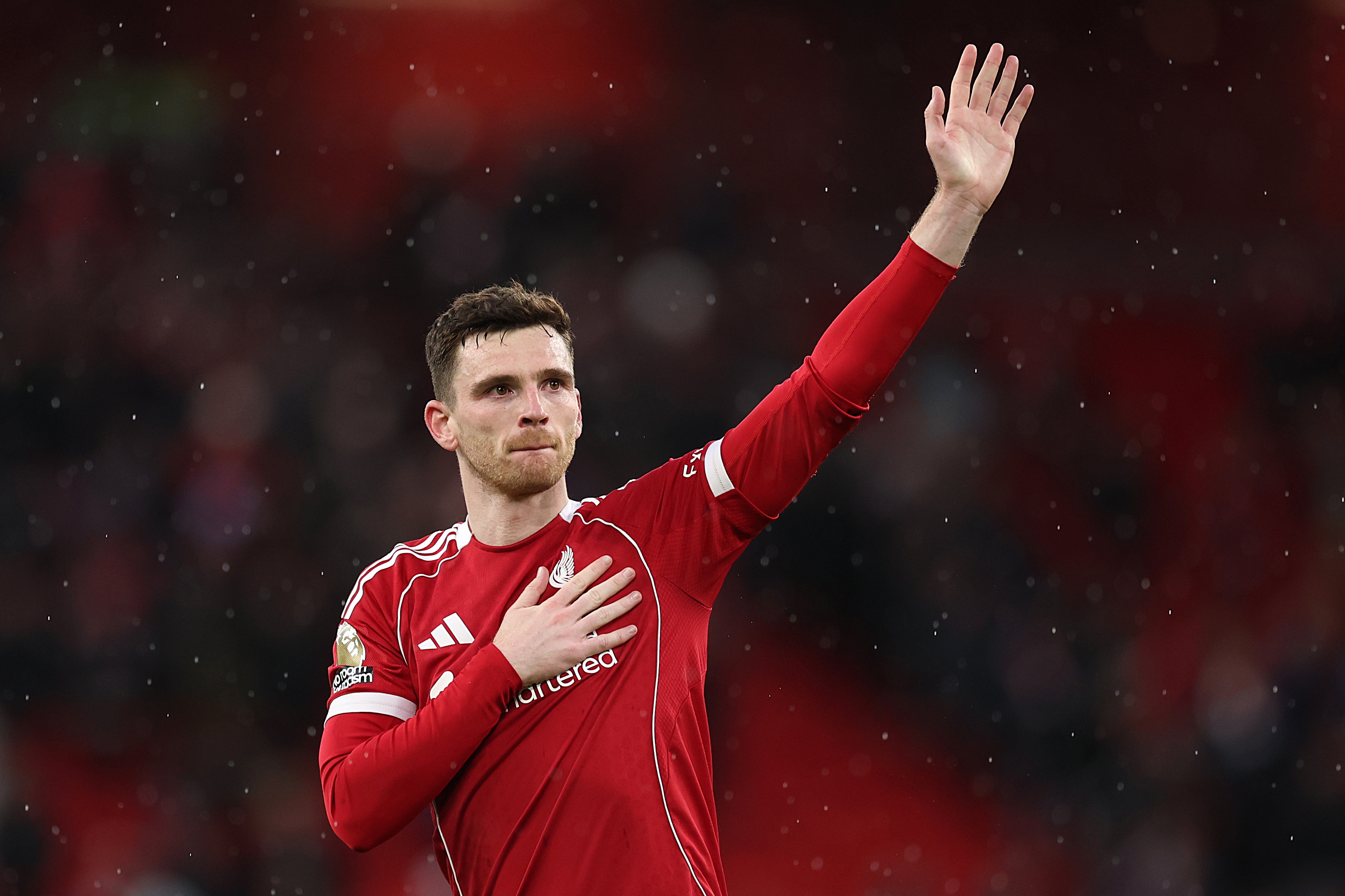 Former Liverpool left-back Andy Robertson raises his left arm and pats the liverbird on his chest.