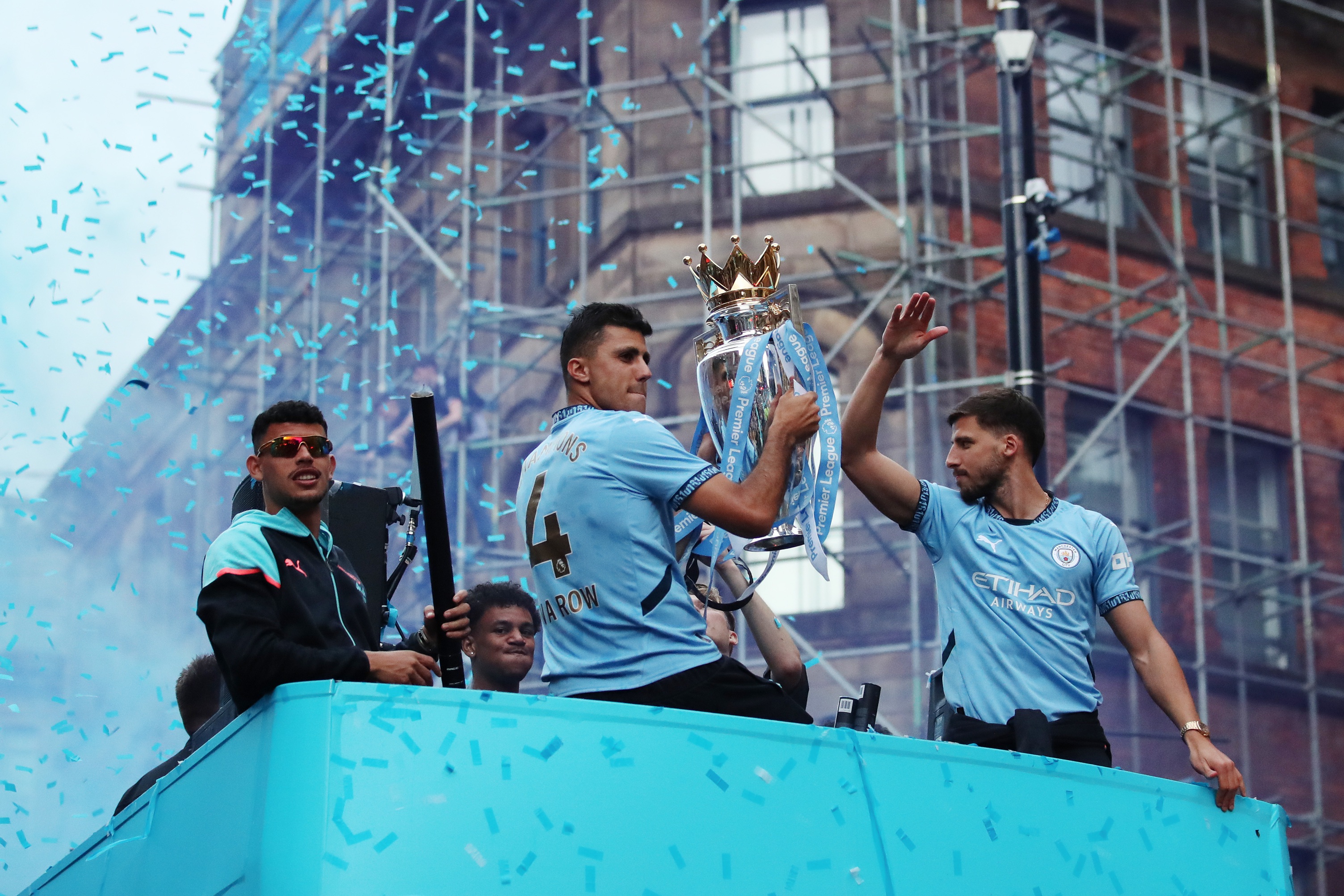 Rodri holds the Premier League trophy on open top bus celebration with Man City teammates.