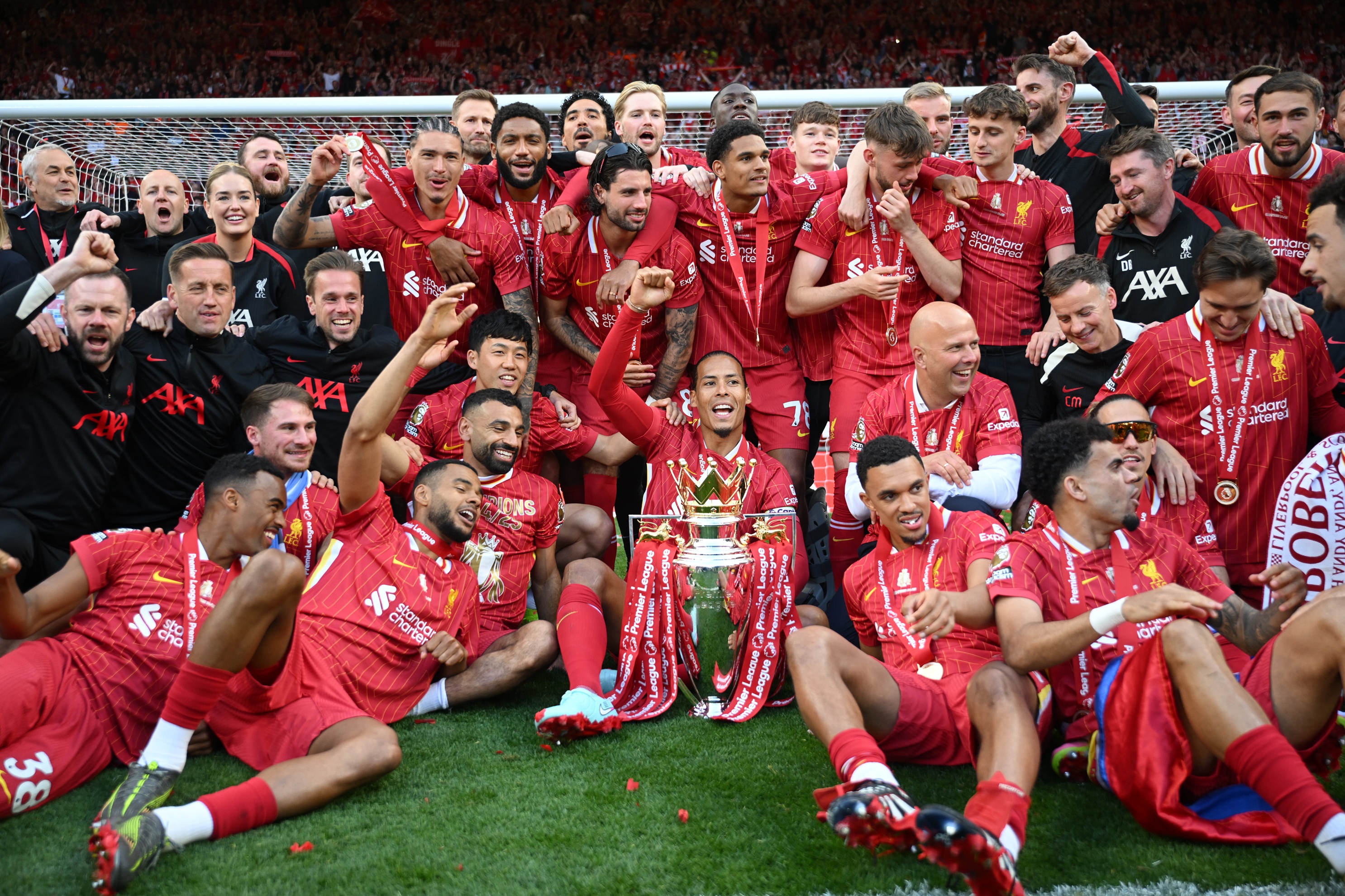 Trent Alexander-Arnold sits on the turf surrounded by Liverpool teammates celebrating.
