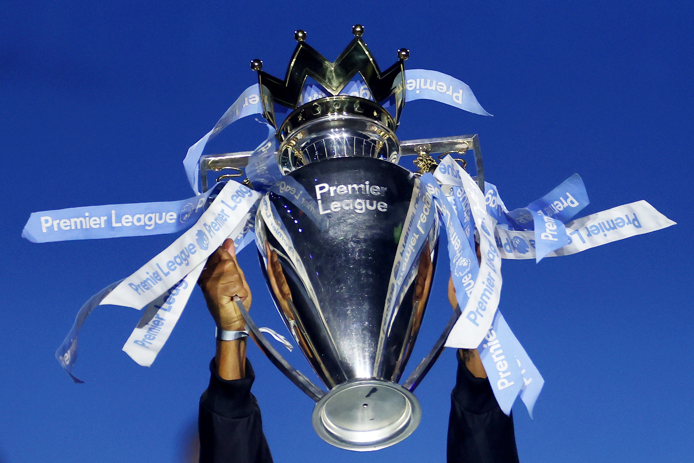 A pair of hands hold up the Premier League trophy.