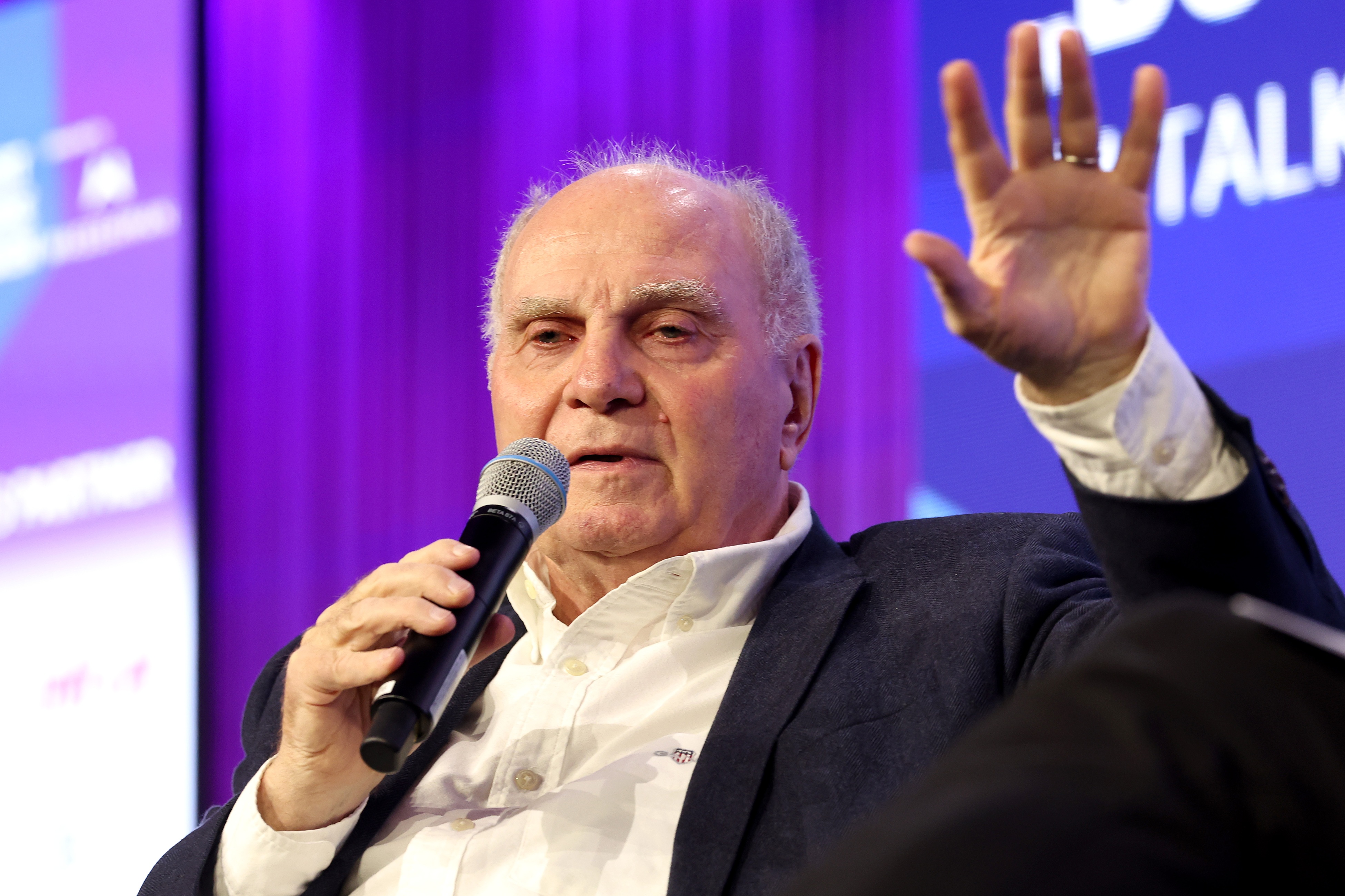 Bayern chief Uli Hoeness raises his hand and holds a microphone.